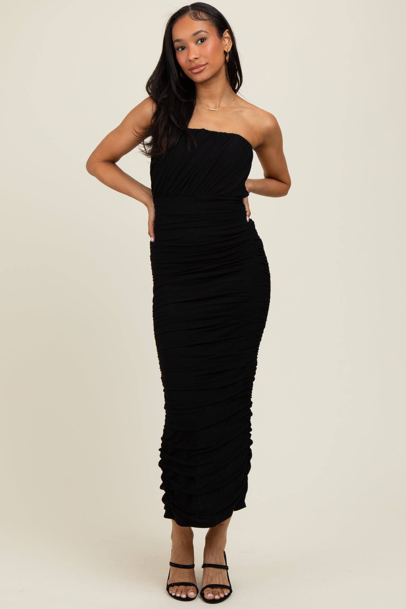 woman wearing a fitted black strapless midi dress with ruching details and a bodycon silhouette