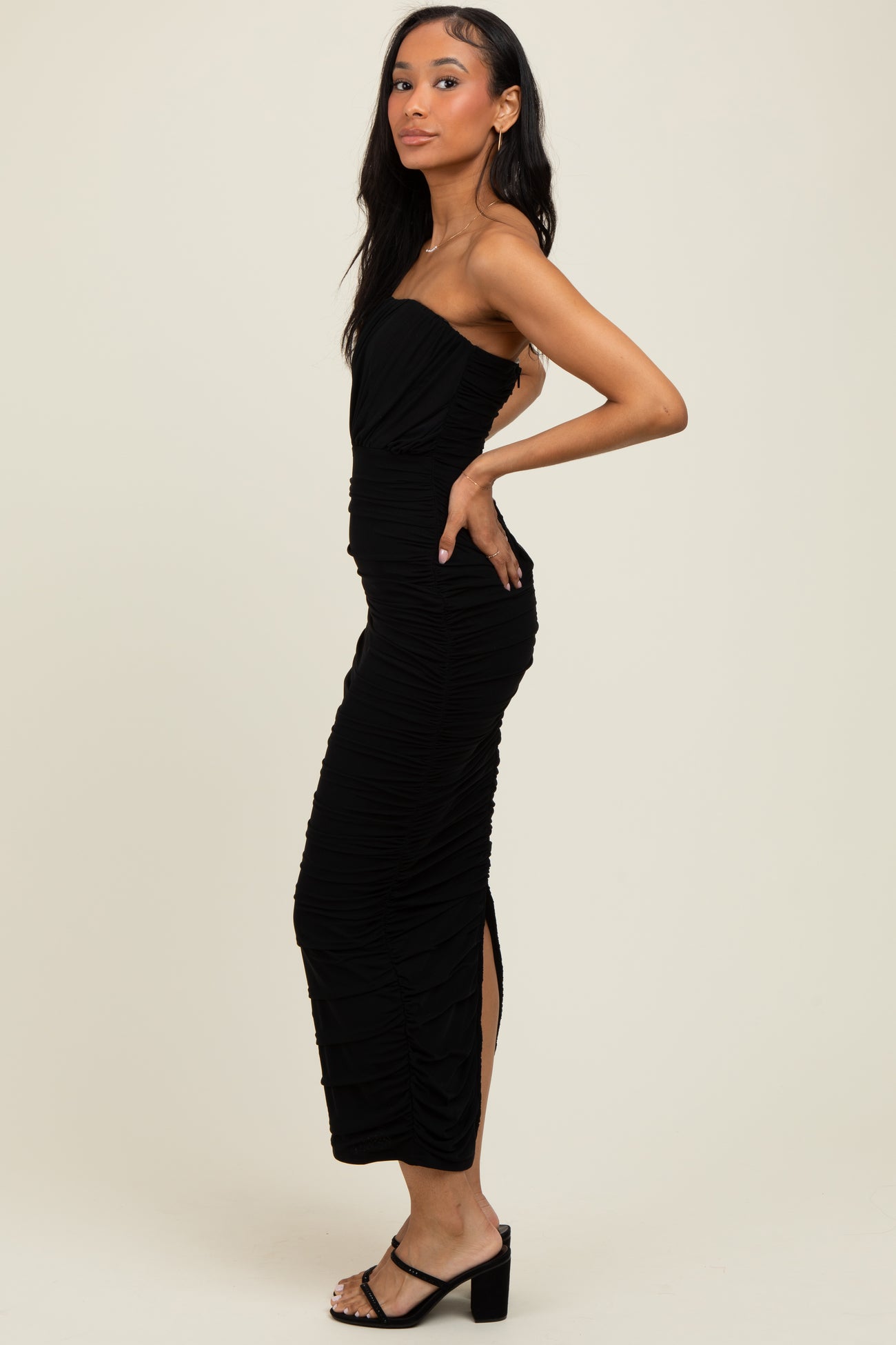 woman wearing a black strapless ruched midi dress with side slits and strappy heeled sandals