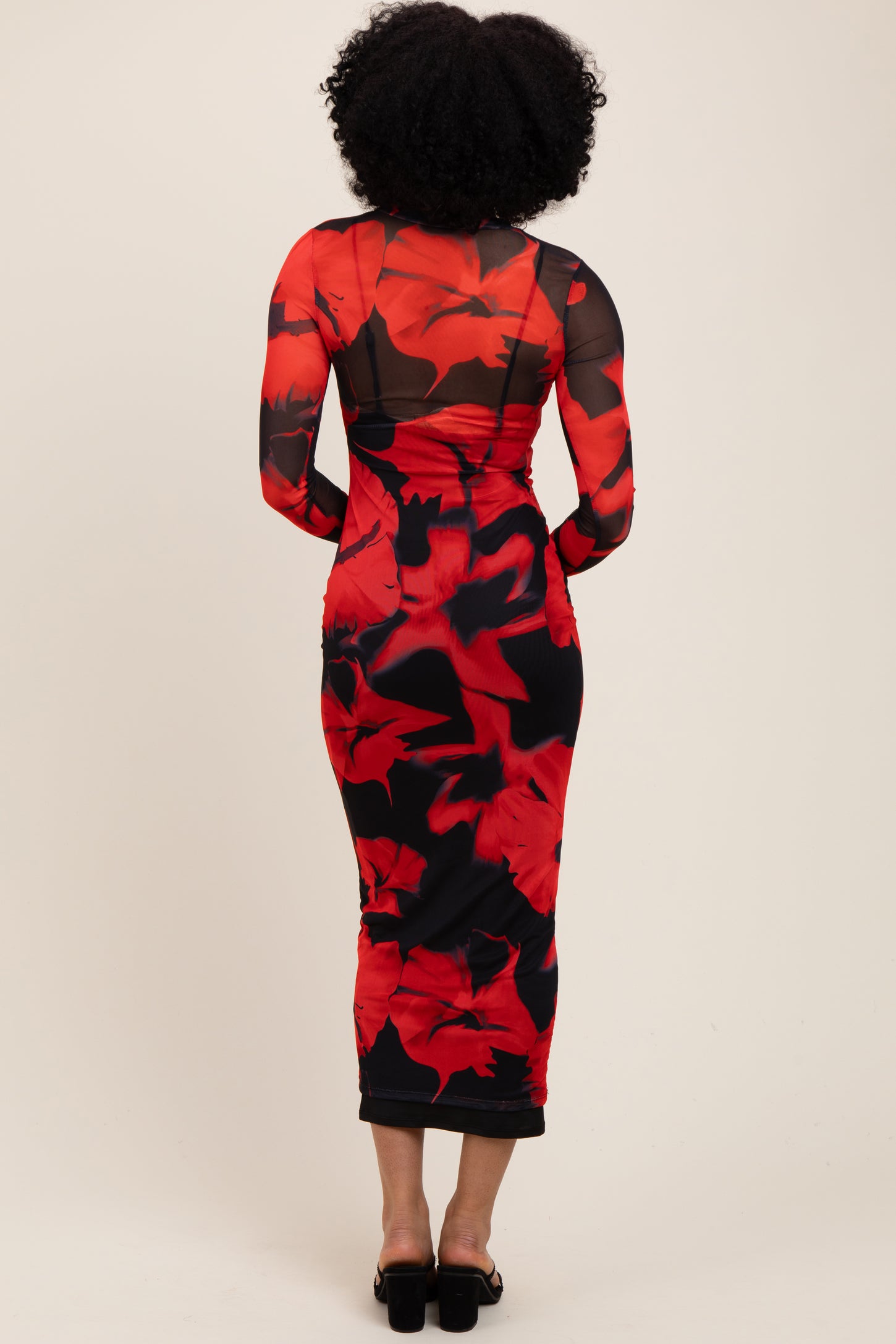 woman wearing a red floral midi dress with long sheer sleeves and a fitted silhouette, view from the back