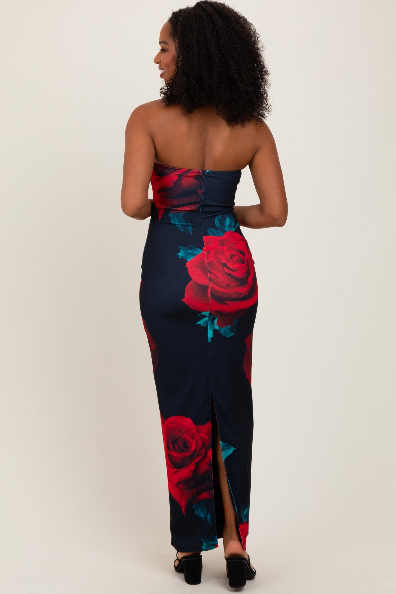 woman wearing a navy blue strapless floral maxi dress with red roses and a thigh-high slit, seen from the back