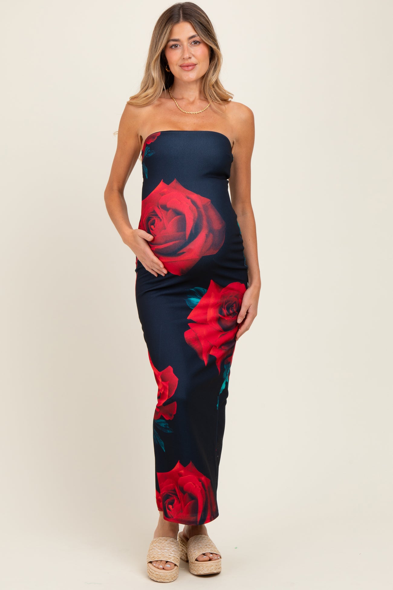 woman wearing a navy blue strapless maternity dress with red rose prints and holding her baby bump