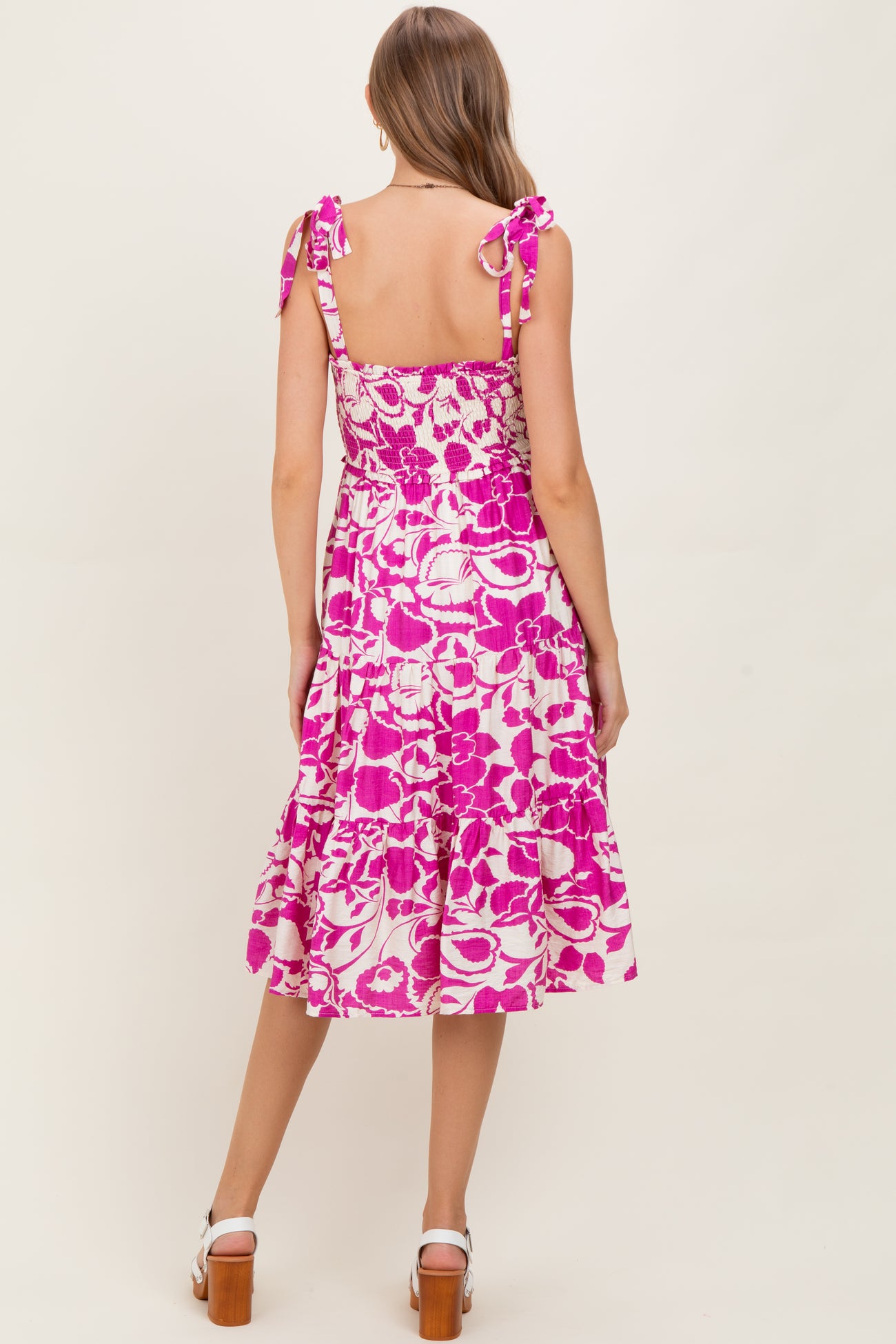 woman wearing a pink floral print maternity dress with tie straps and a tiered skirt, showing her baby bump