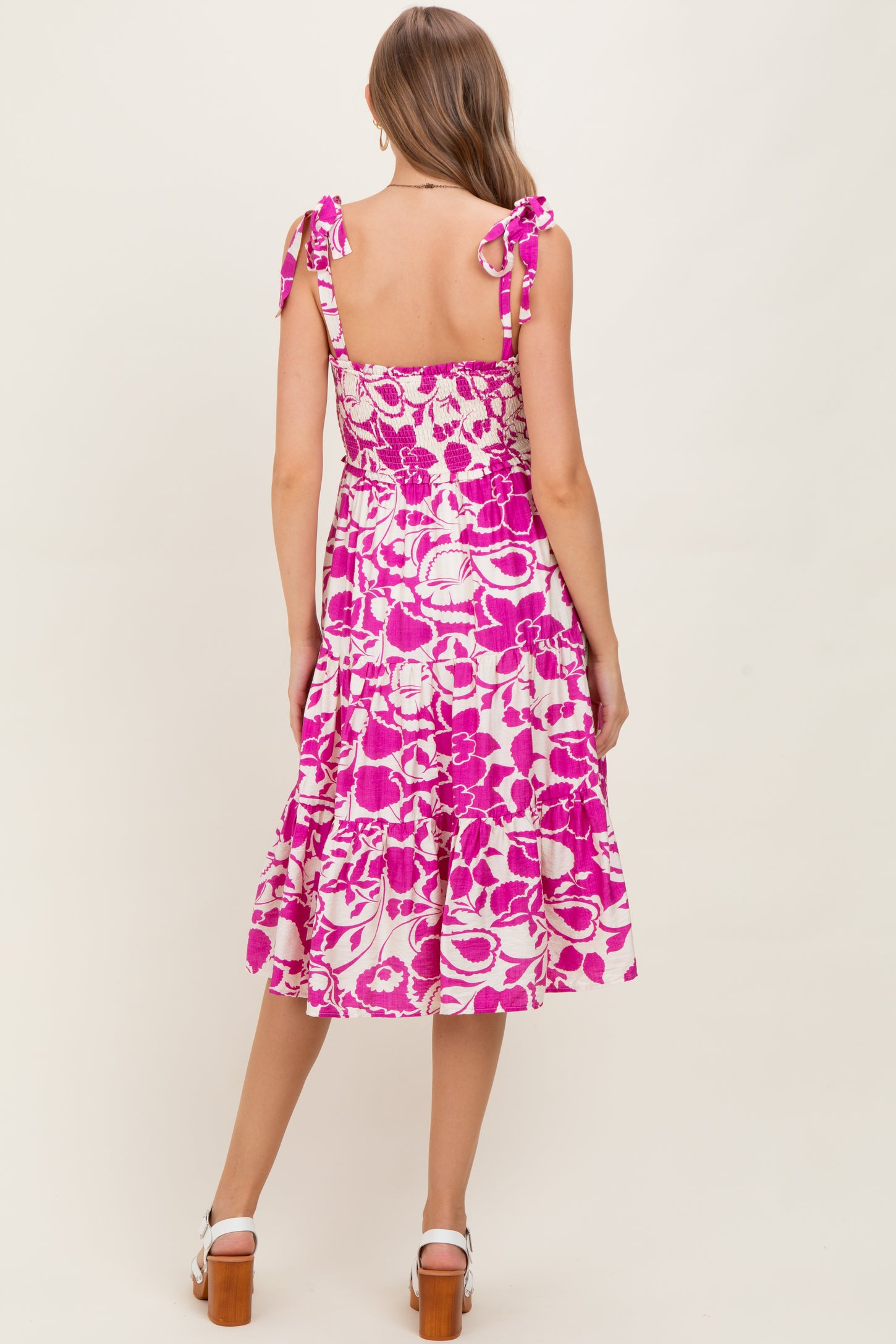 woman wearing a pink floral print maternity dress with tie straps and a tiered skirt, showing her baby bump