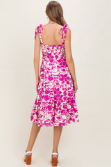woman wearing a pink floral print maternity dress with tie straps and a tiered skirt, showing her baby bump