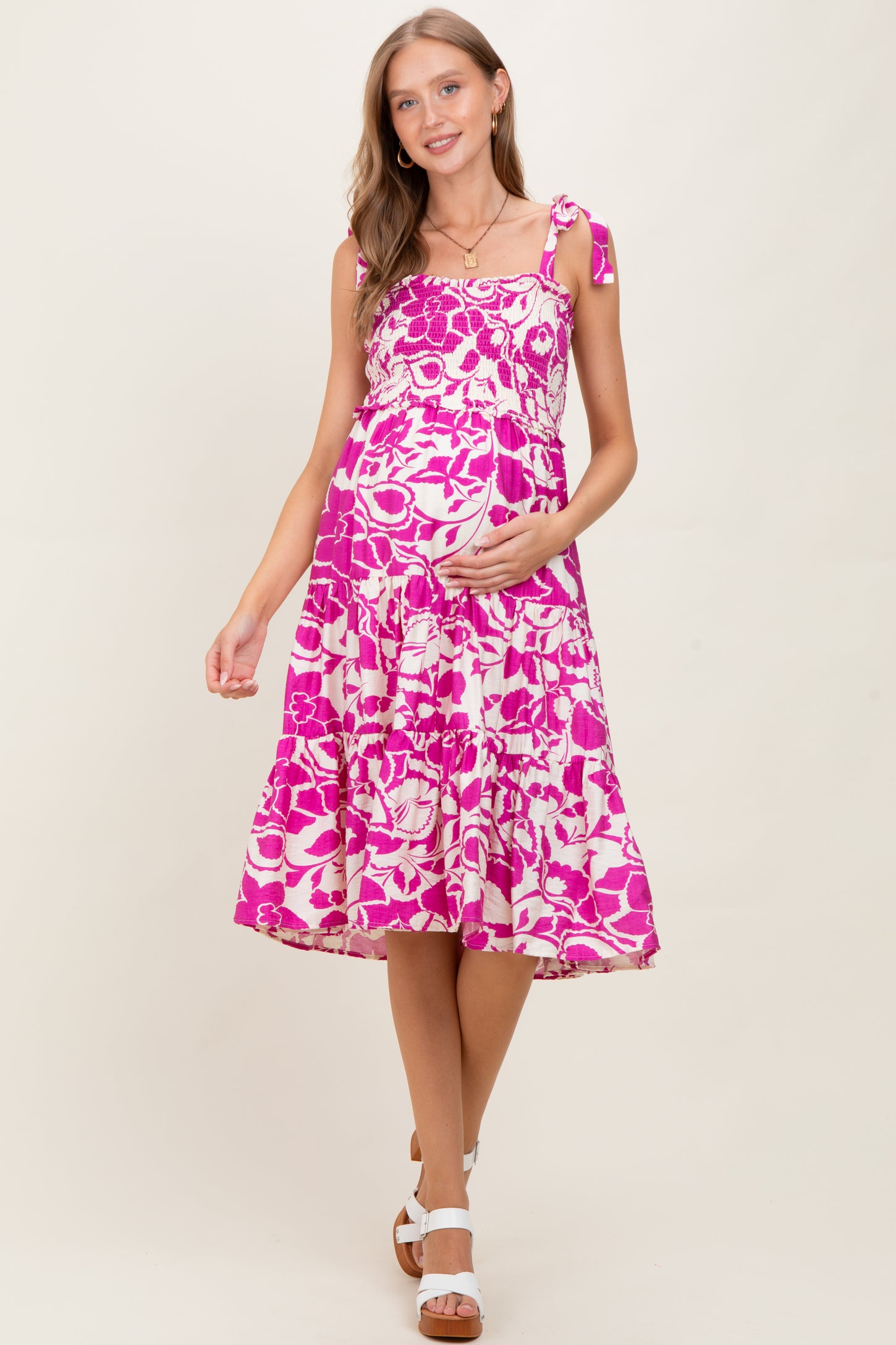 woman wearing a pink floral maternity dress with tie straps and a visible baby bump