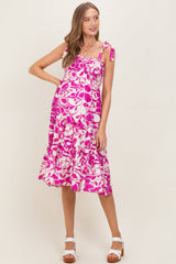 woman wearing a pink floral maternity dress with ruffled details and tie straps, showing her baby bump