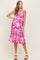 woman wearing a pink floral maternity dress with ruffled details and tie straps, showing her baby bump