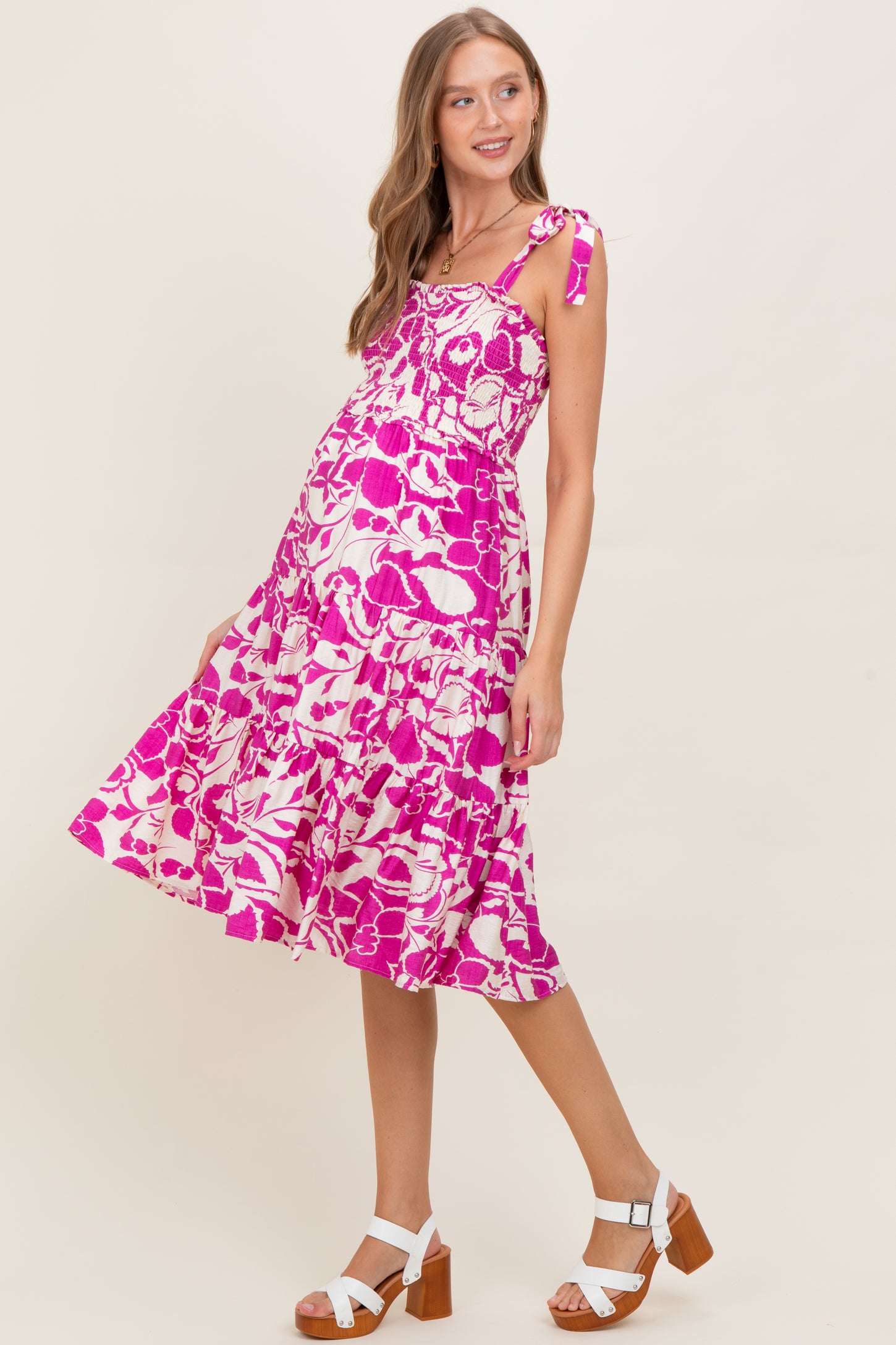 woman wearing a pink and white floral maternity dress with tie straps and a flowing skirt, showing her baby bump