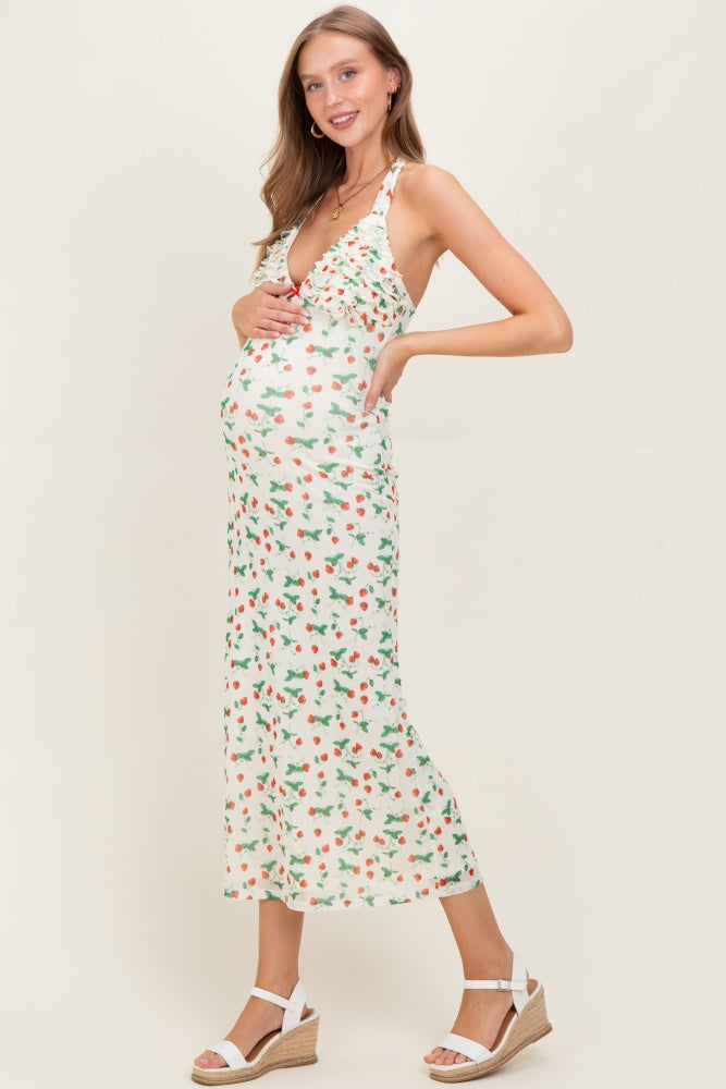 woman wearing a white floral maternity dress with a halter neck, showcasing her baby bump and styled with wedge sandals