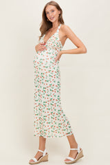 woman wearing a white floral maternity dress with a halter neck, showcasing her baby bump and styled with wedge sandals