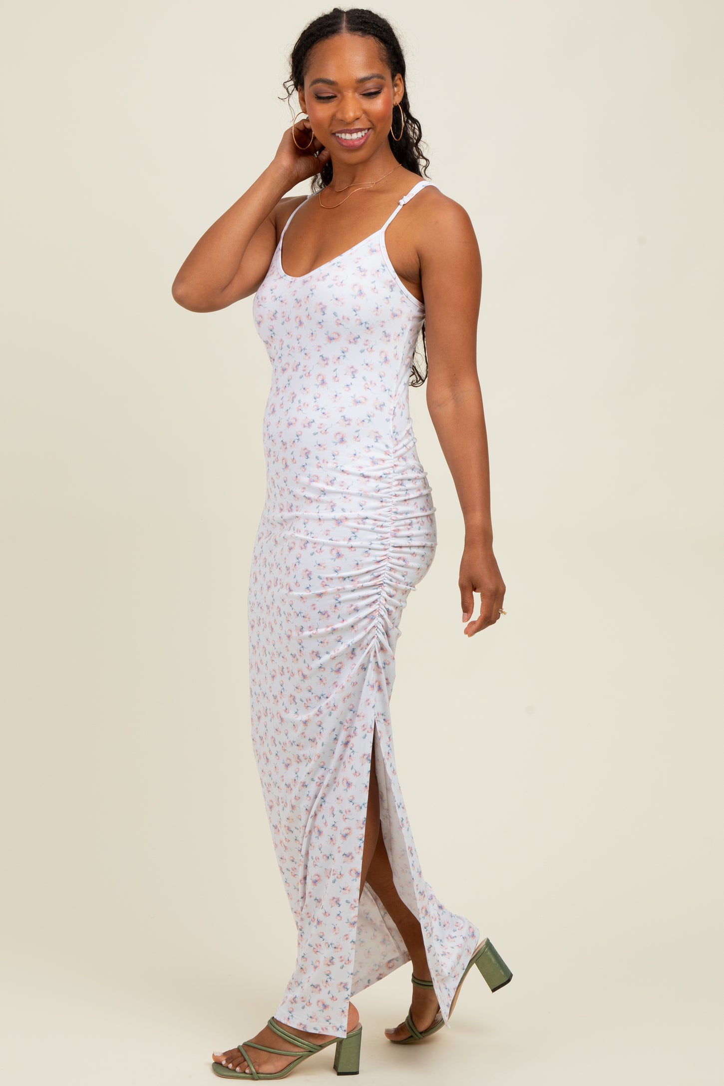 woman wearing a white floral maxi dress with side ruching and a thigh-high slit, paired with green heeled sandals