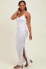 woman wearing a white floral maxi dress with side ruching and a thigh-high slit, paired with green heeled sandals