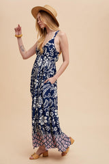 woman wearing a navy blue floral maxi dress with pockets and a straw hat, posing against a beige background