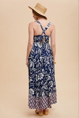 women wearing a navy blue floral maxi dress with a crisscross back and pink patterned hem, styled with a straw hat