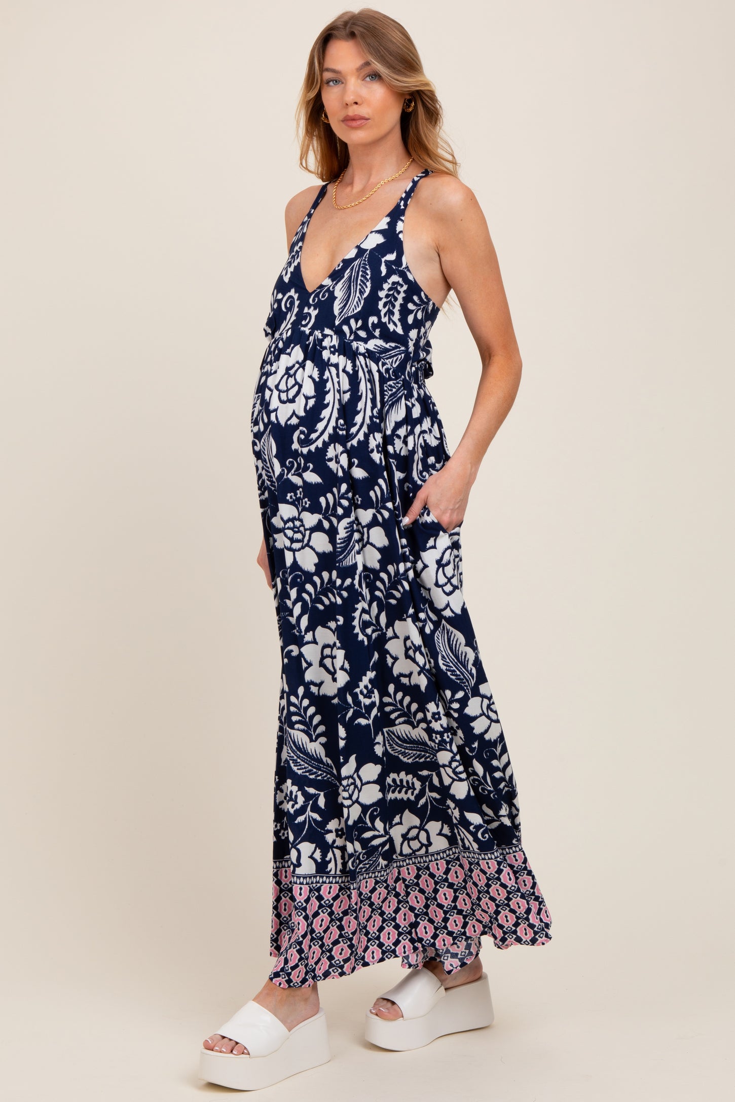 woman wearing a navy floral maternity maxi dress with a v-neckline and side pockets, showcasing her baby bump