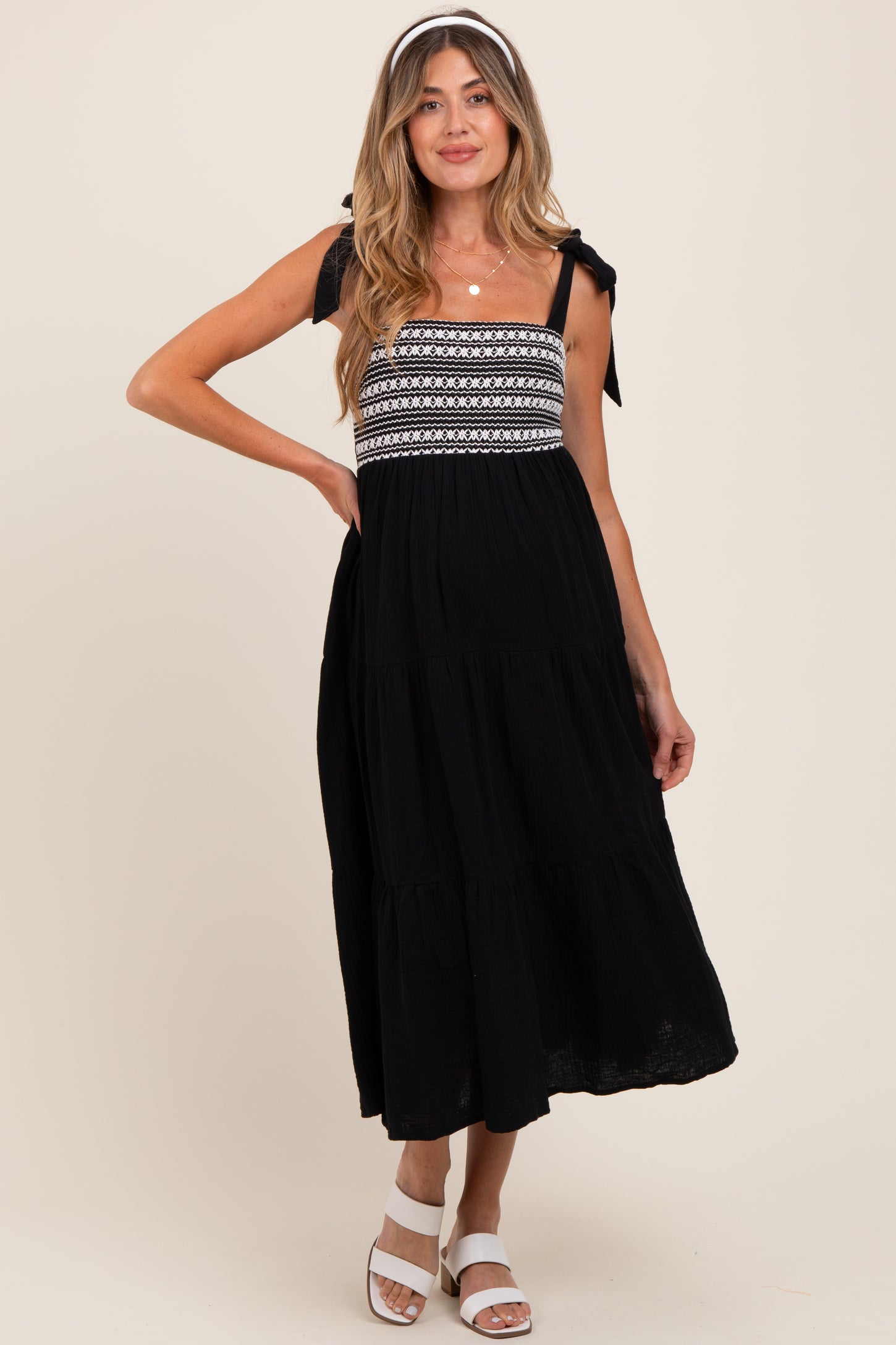 woman wearing a black maternity dress with embroidered bodice and tie straps, featuring a flowy tiered skirt