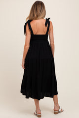 woman wearing a black maternity midi dress with tie straps and a smocked bodice, showing a pregnant belly