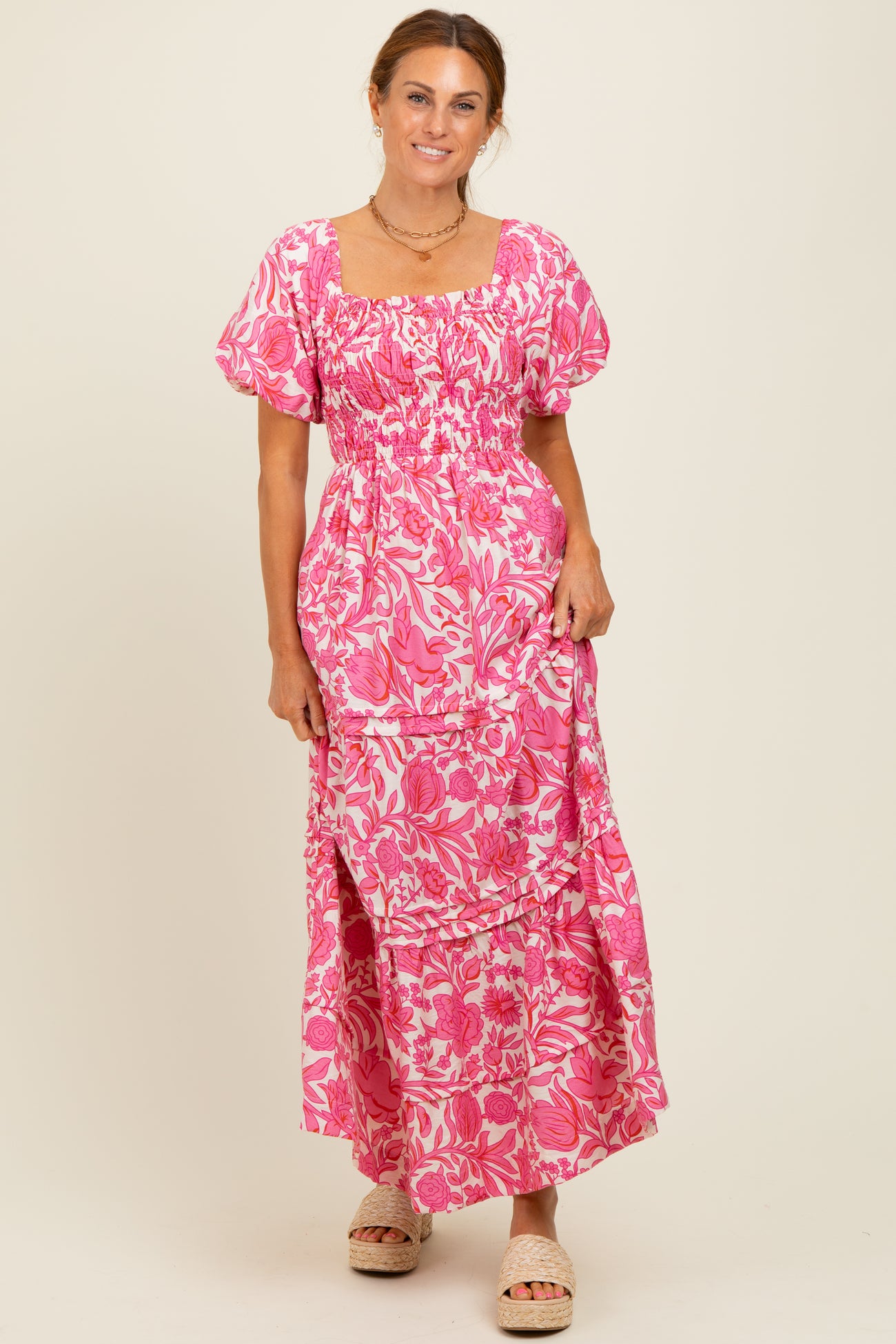 woman wearing a pink floral maxi dress with puff sleeves and a square neckline, standing and smiling