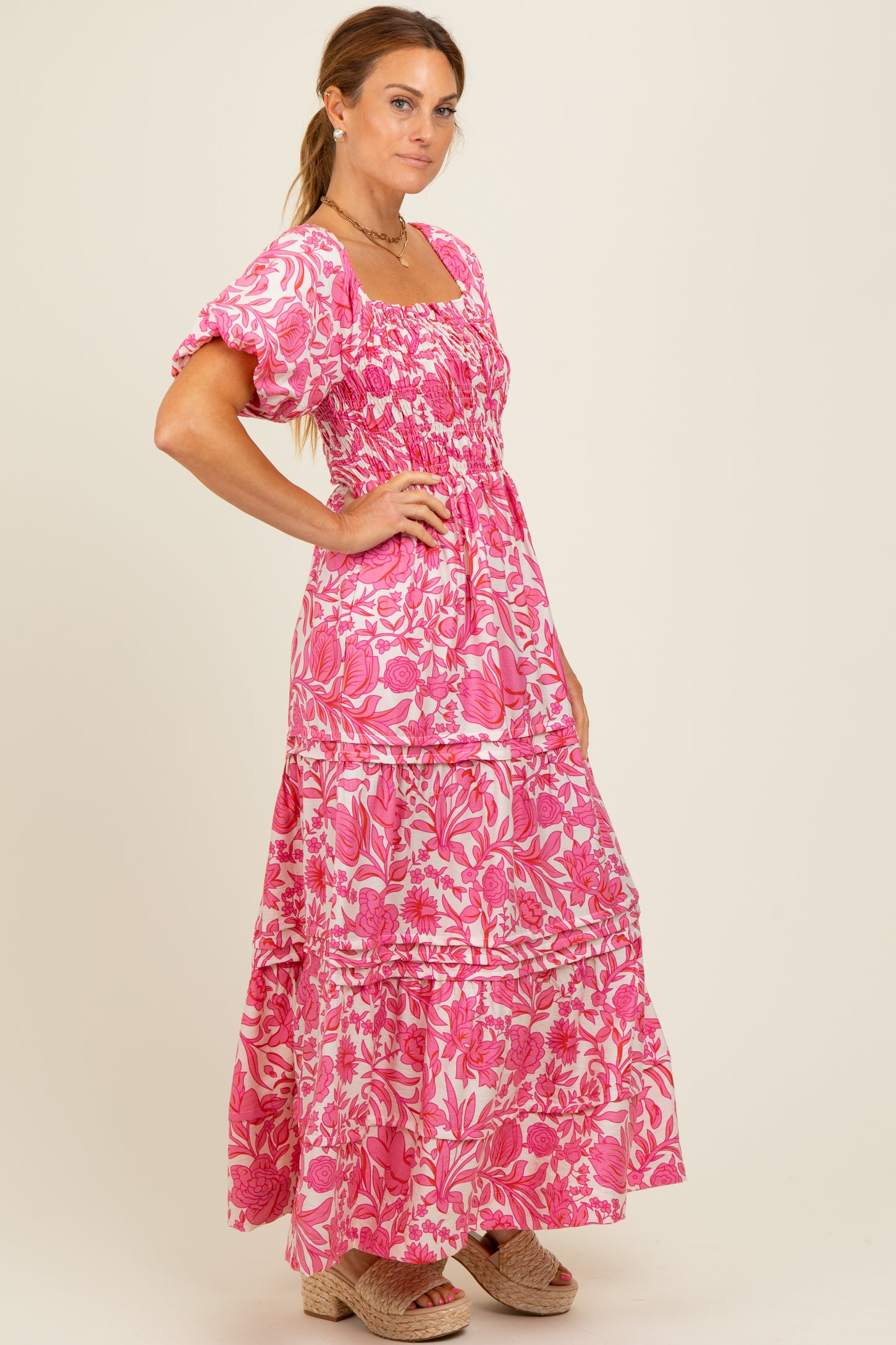 woman wearing a pink floral maxi dress with puff sleeves and a tiered skirt, styled with light-colored wedges