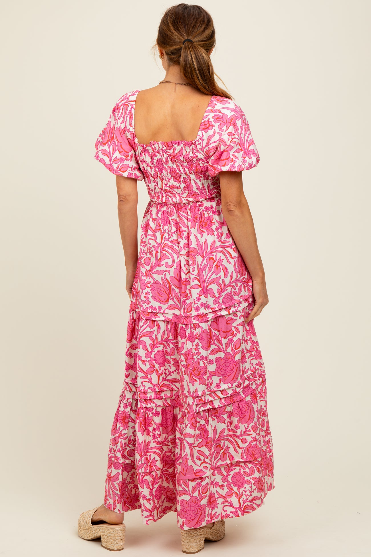 woman wearing a pink floral maxi dress with puff sleeves and a tiered skirt, photographed from the back
