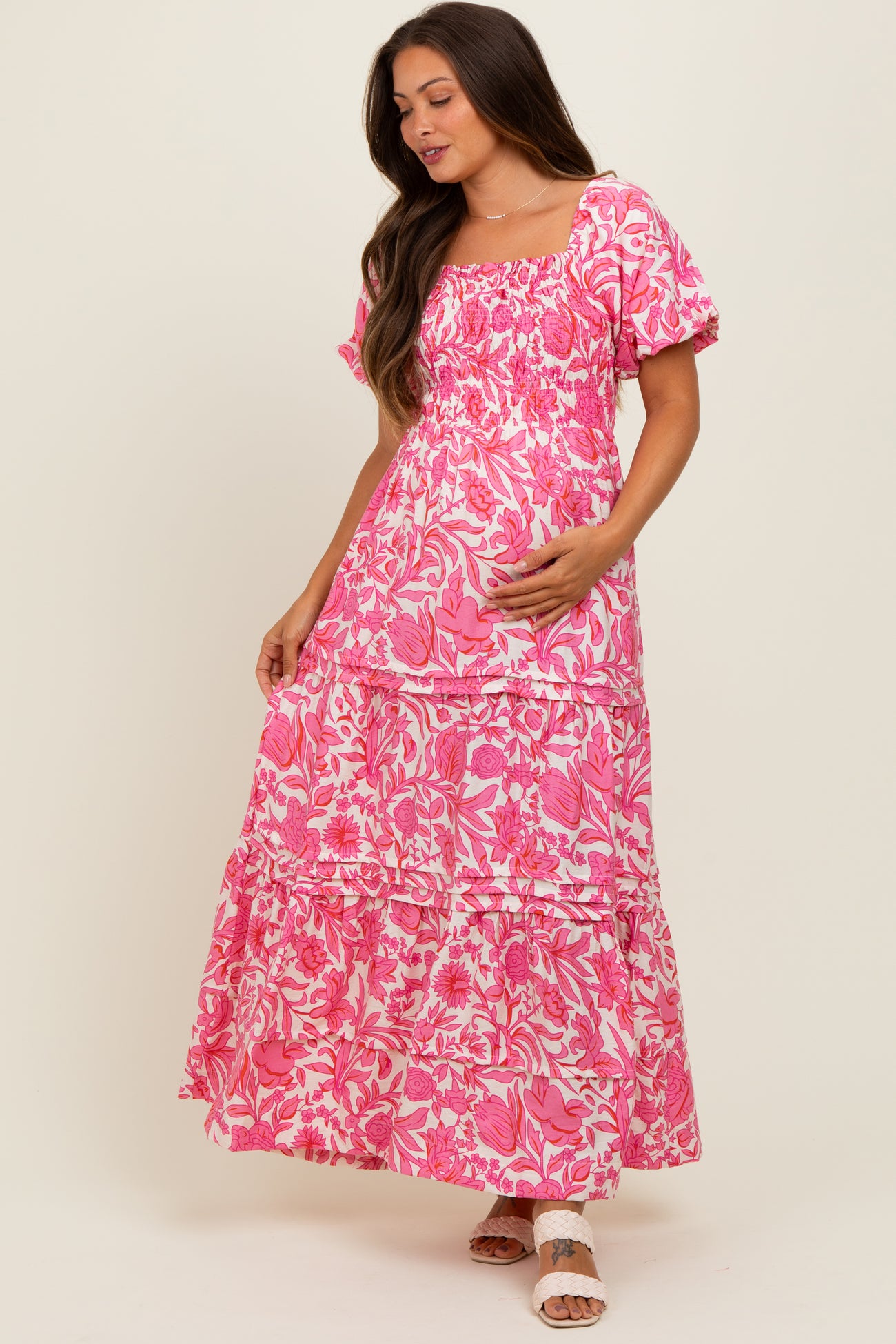 woman wearing a pink floral maternity maxi dress with puff sleeves and a tiered skirt, gently holding her baby bump