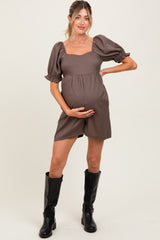 woman wearing a brown checkered maternity romper with puff sleeves and holding her baby bump