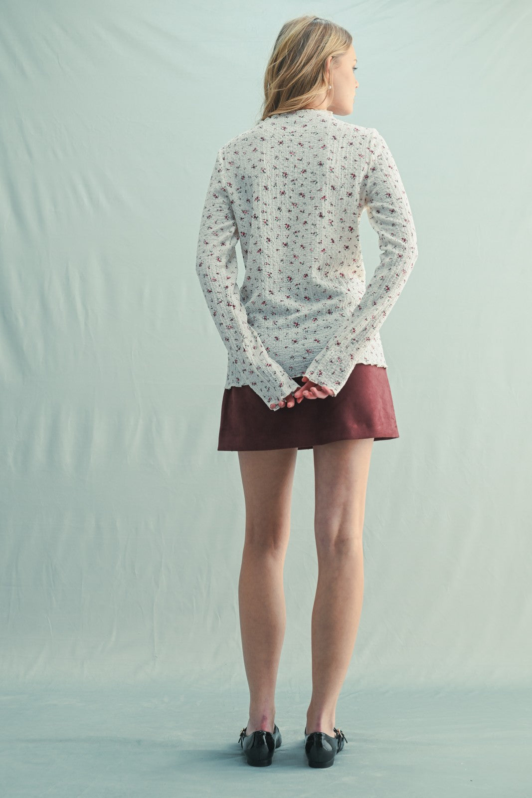 woman wearing a cream floral long sleeve sweater with a maroon skirt, viewed from the back
