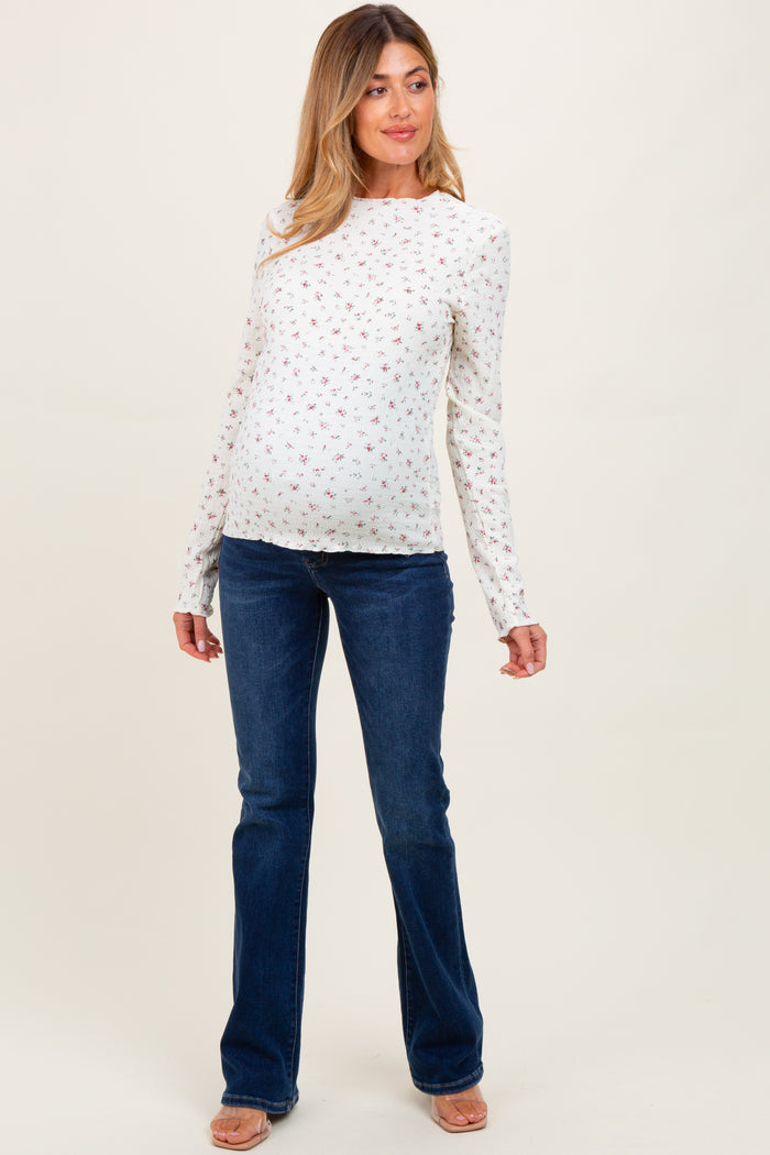 woman wearing a white floral long sleeve maternity top and blue flared jeans, showcasing her baby bump