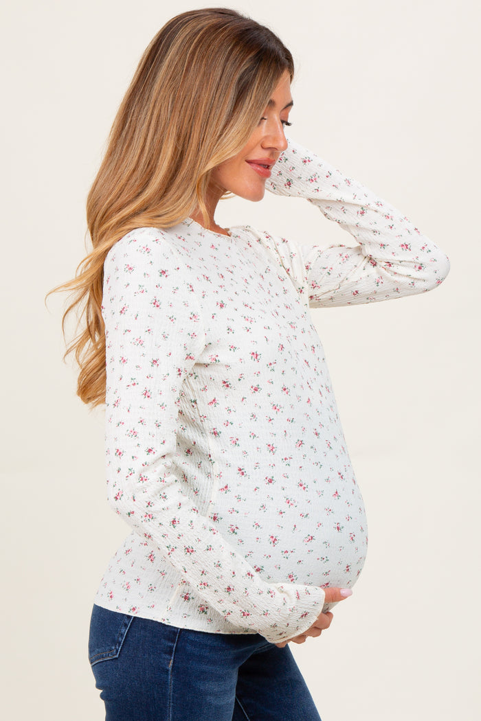 woman wearing a light blue maternity sweater with floral patterns and holding her baby bump