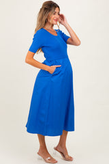 woman wearing a bright blue maternity dress with short sleeves, a fitted top, and a flowing skirt, showing a baby bump