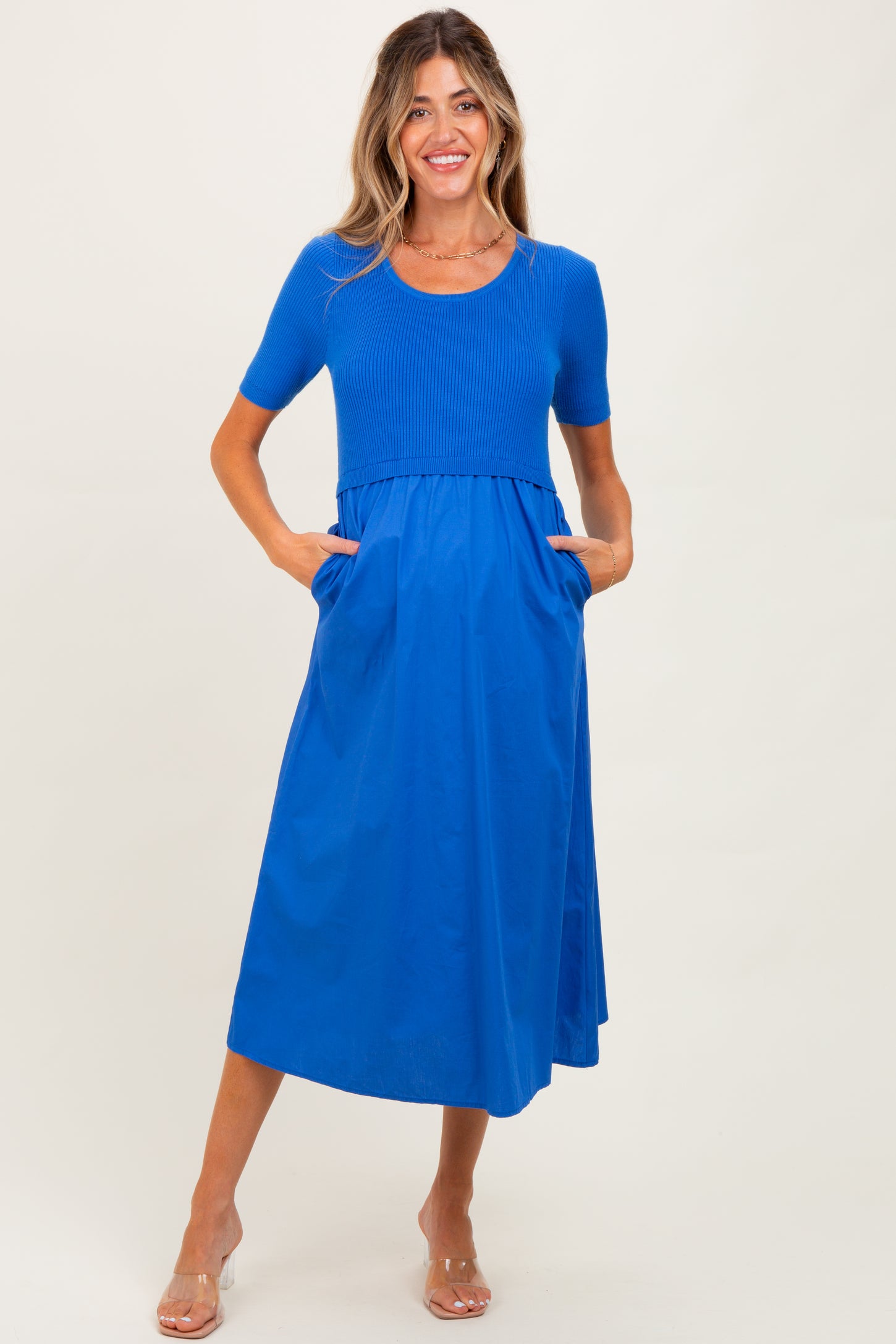 woman wearing a bright blue maternity dress with a ribbed bodice and flowy skirt, featuring pockets
