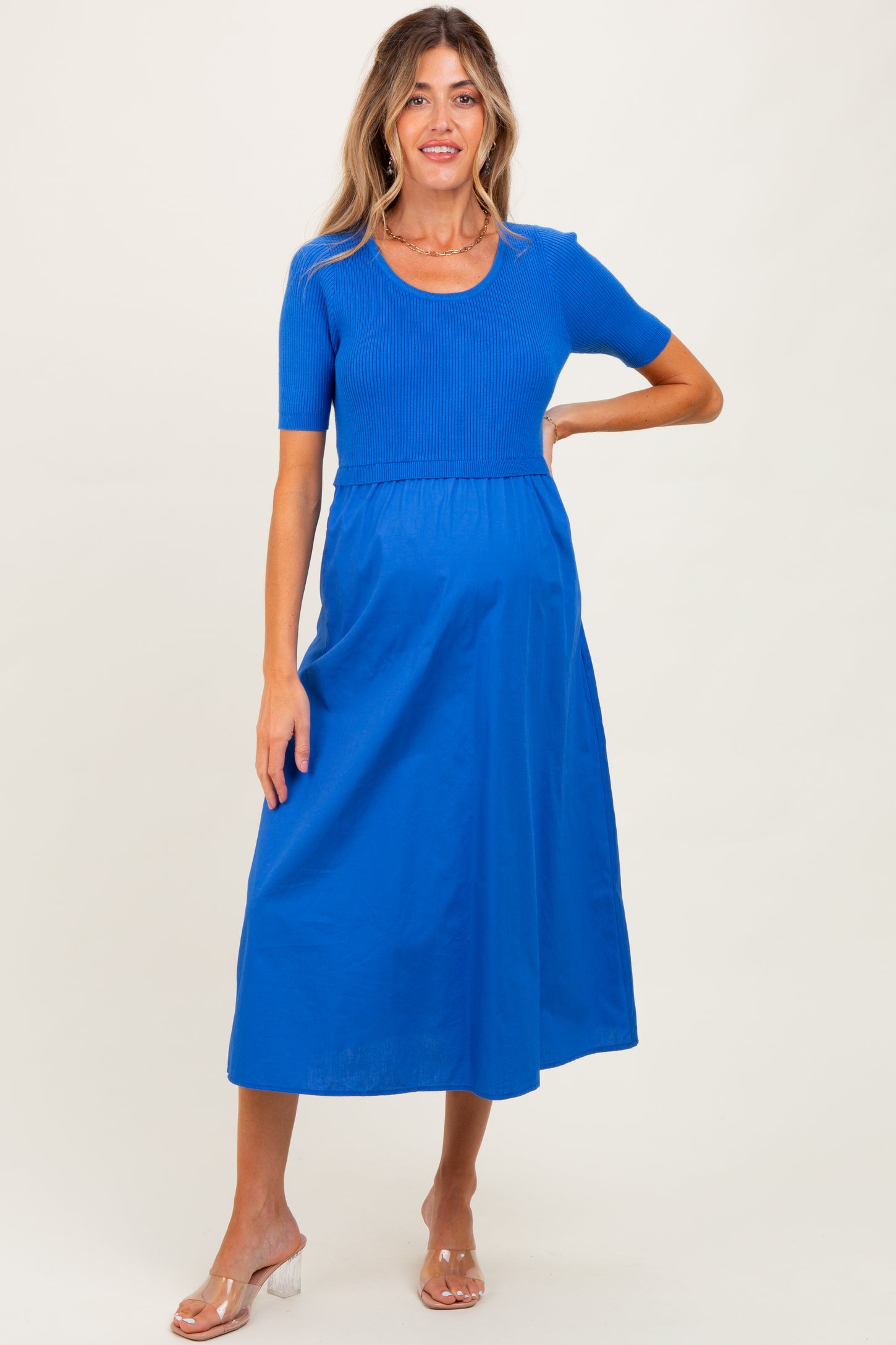 woman wearing a bright blue short sleeve maternity dress with a ribbed top and flowing skirt, baby bump visible