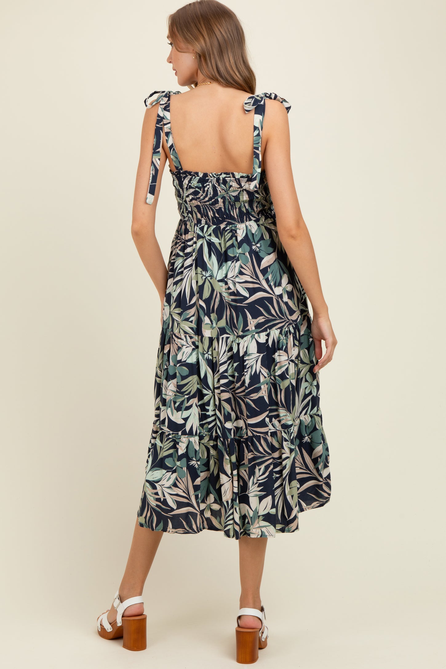 woman wearing a navy floral maternity dress with tie shoulder straps and a tiered skirt, showing a baby bump