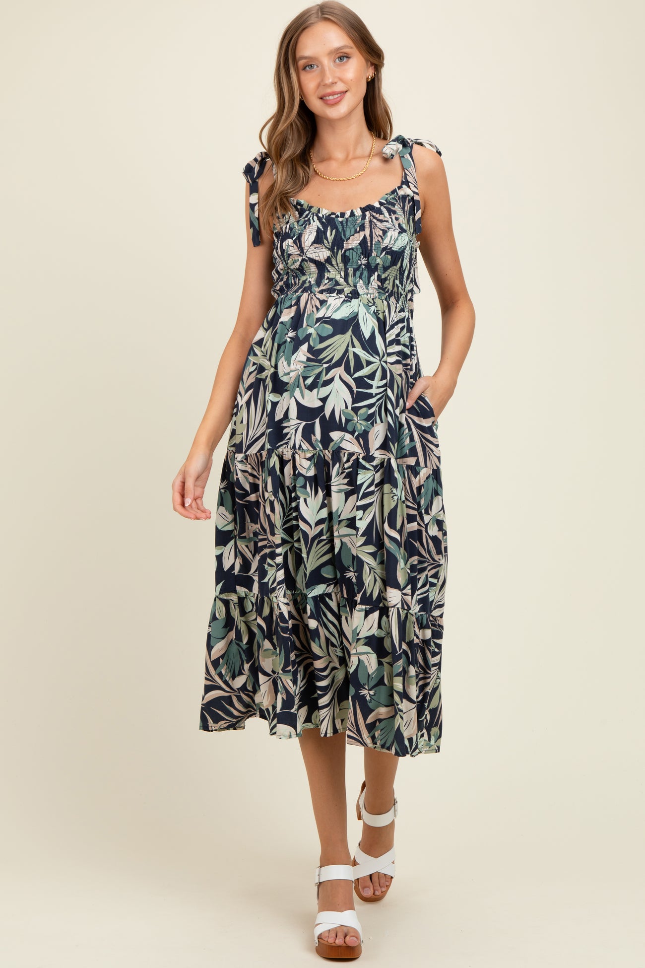 woman wearing a dark floral print maternity dress with tie shoulder straps and pockets, showing her baby bump