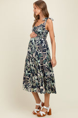 woman wearing a navy floral maternity dress with tie straps, holding her baby bump