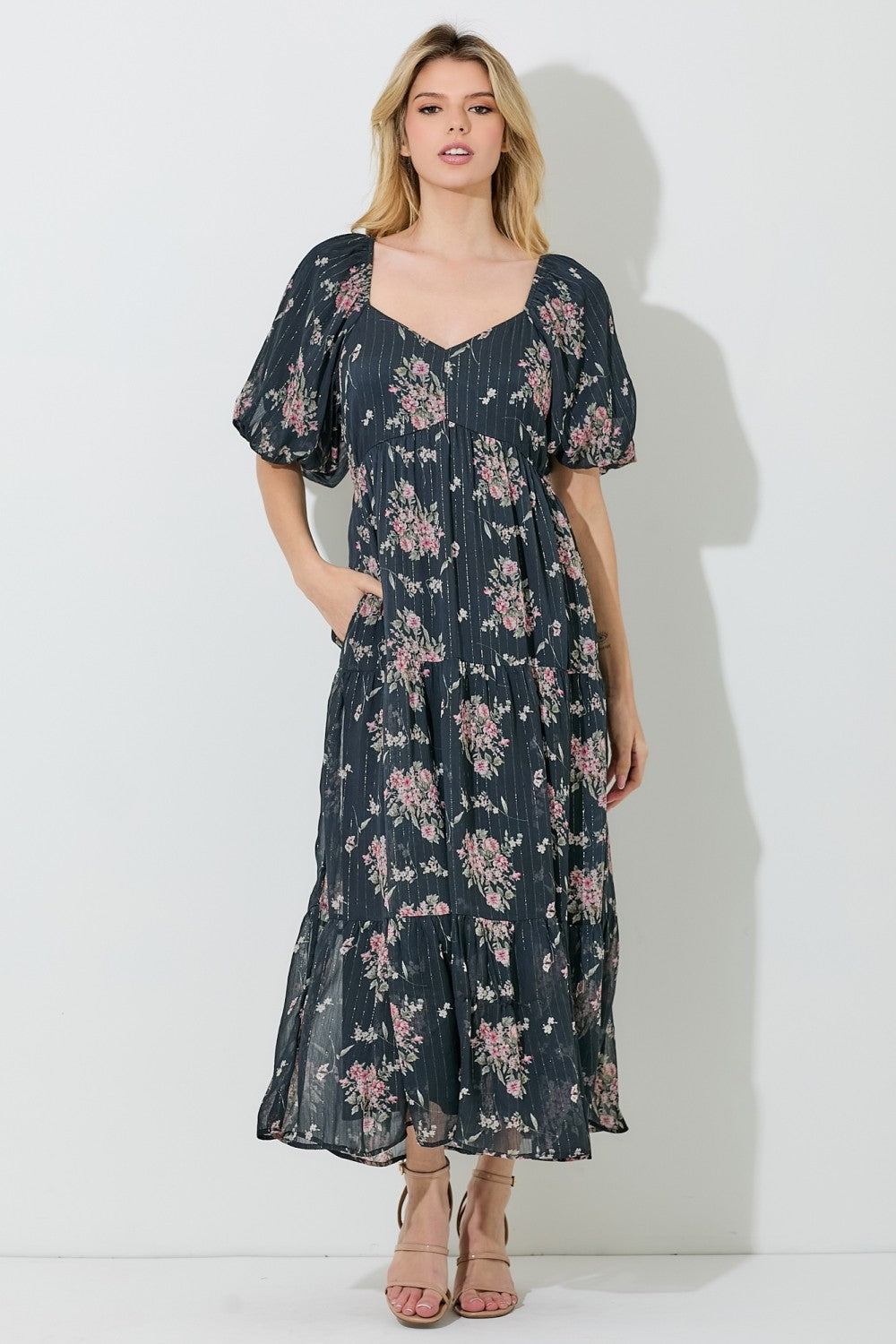 woman wearing a navy floral maxi dress with puff sleeves and pockets, standing against a light backdrop