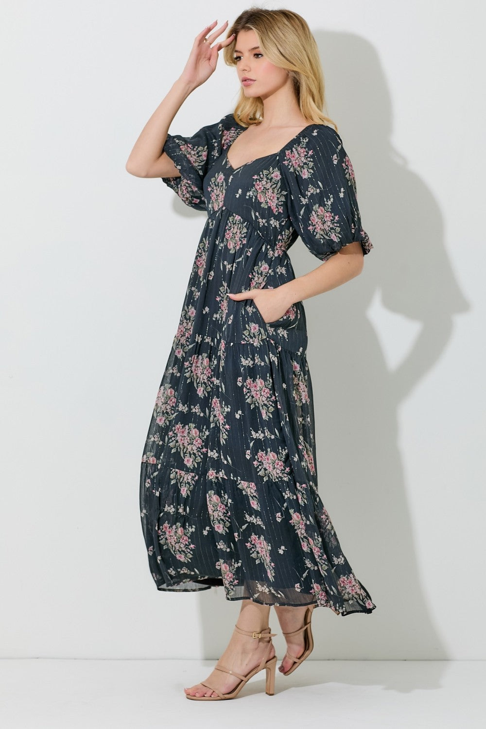 woman wearing a navy blue floral maxi dress with puff sleeves and pockets, standing against a white background