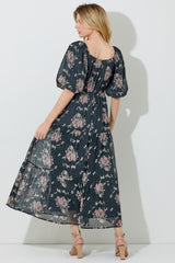 woman wearing a navy floral maxi dress with puff sleeves and ruffled hem, shown from the back