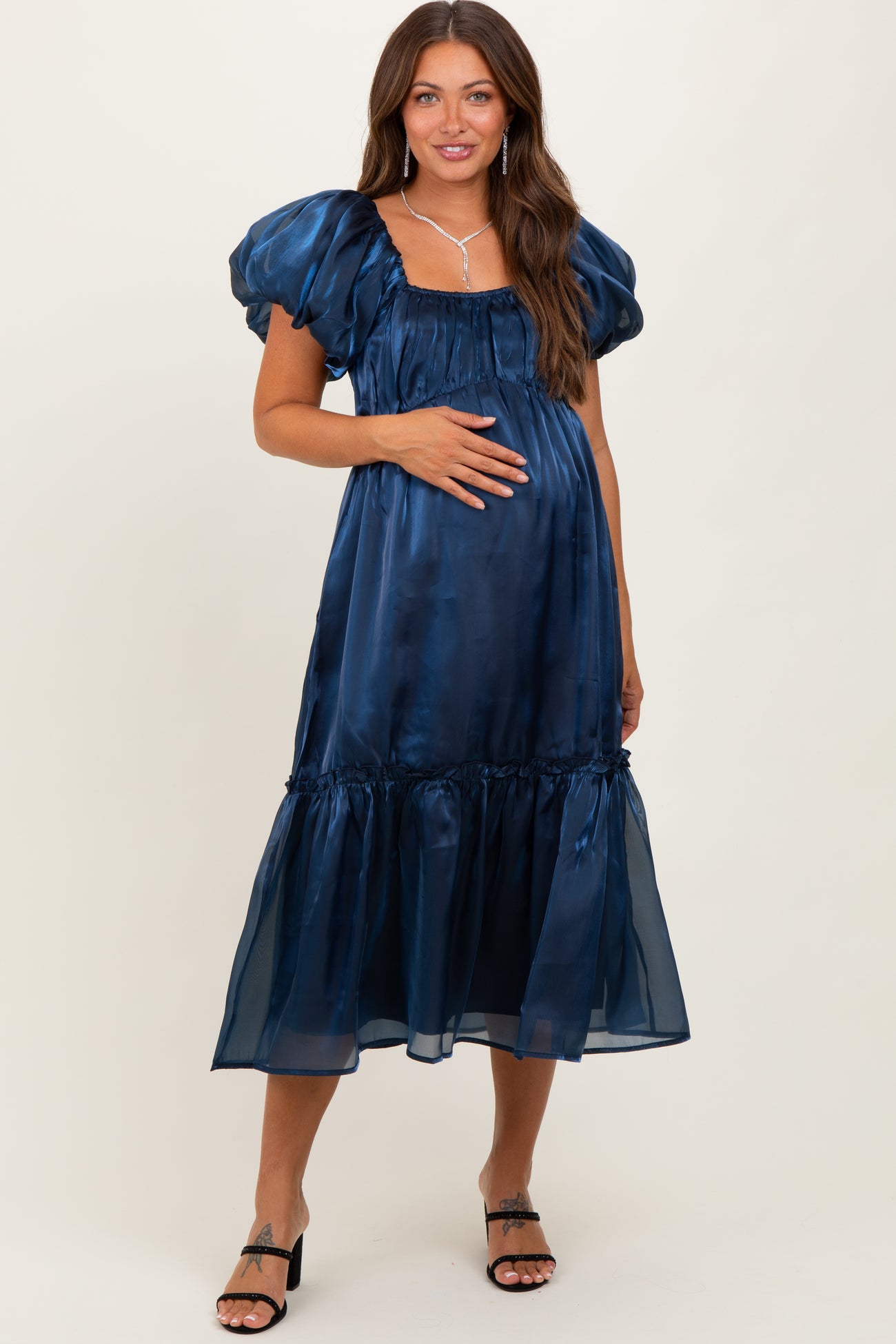 woman wearing a navy blue maternity dress with puff sleeves and a tiered hem, gently holding her baby bump