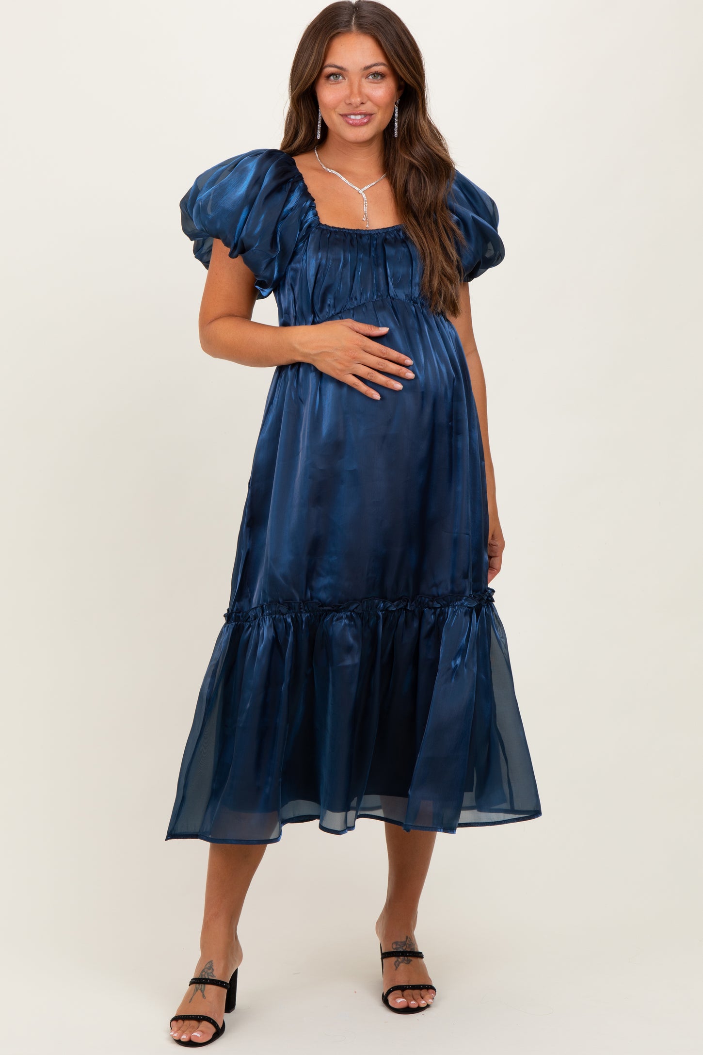 woman wearing a navy blue maternity dress with puff sleeves and a tiered hem, gently holding her baby bump