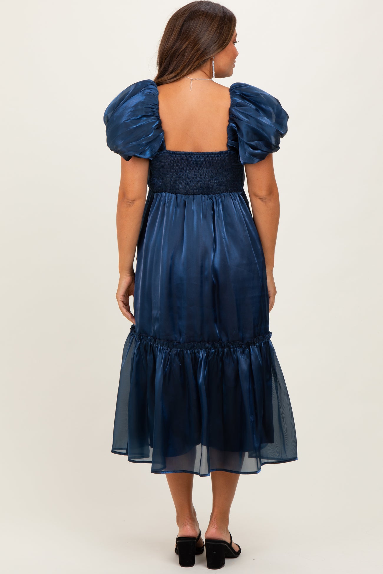 woman wearing a navy blue maternity dress with puff sleeves and a tiered skirt, showcasing a smocked back design