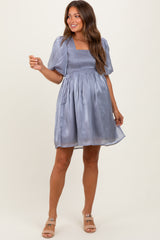 woman wearing a light lavender maternity dress with puff sleeves and a smocked bodice, smiling and posing