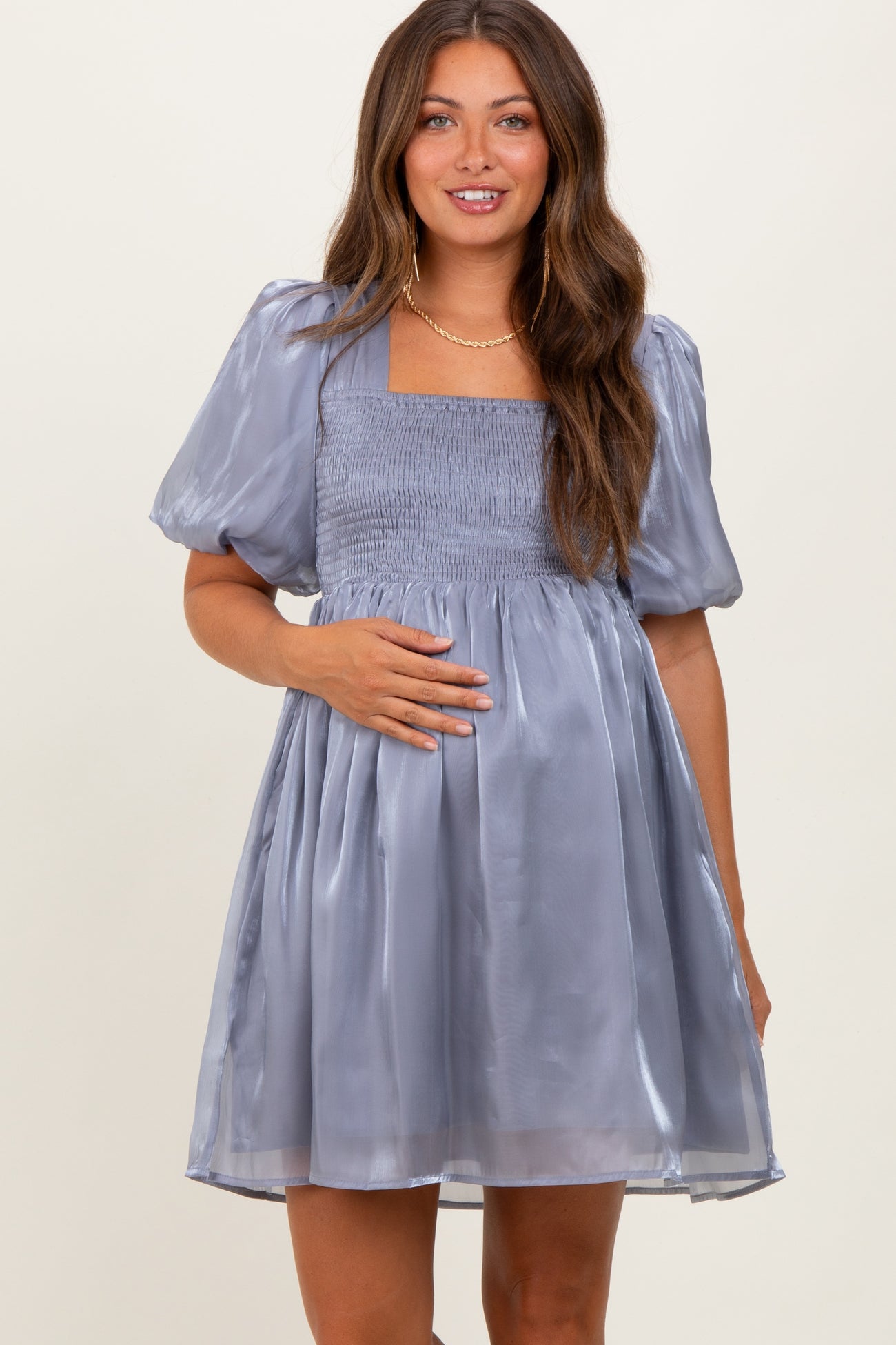 woman wearing a light gray puff sleeve maternity dress with a square neckline and smocked bodice, showing her baby bump