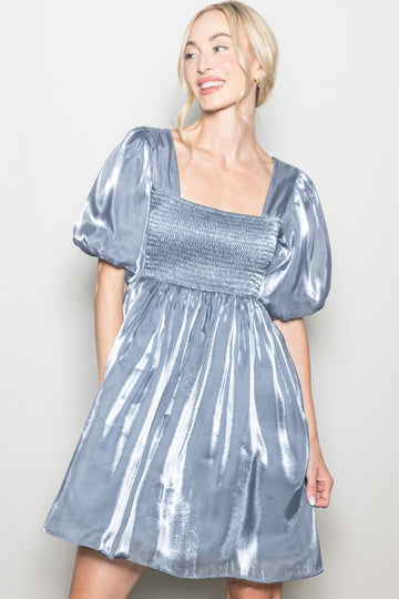 woman wearing a silver smocked dress with puff sleeves and a mini length, smiling against a neutral background