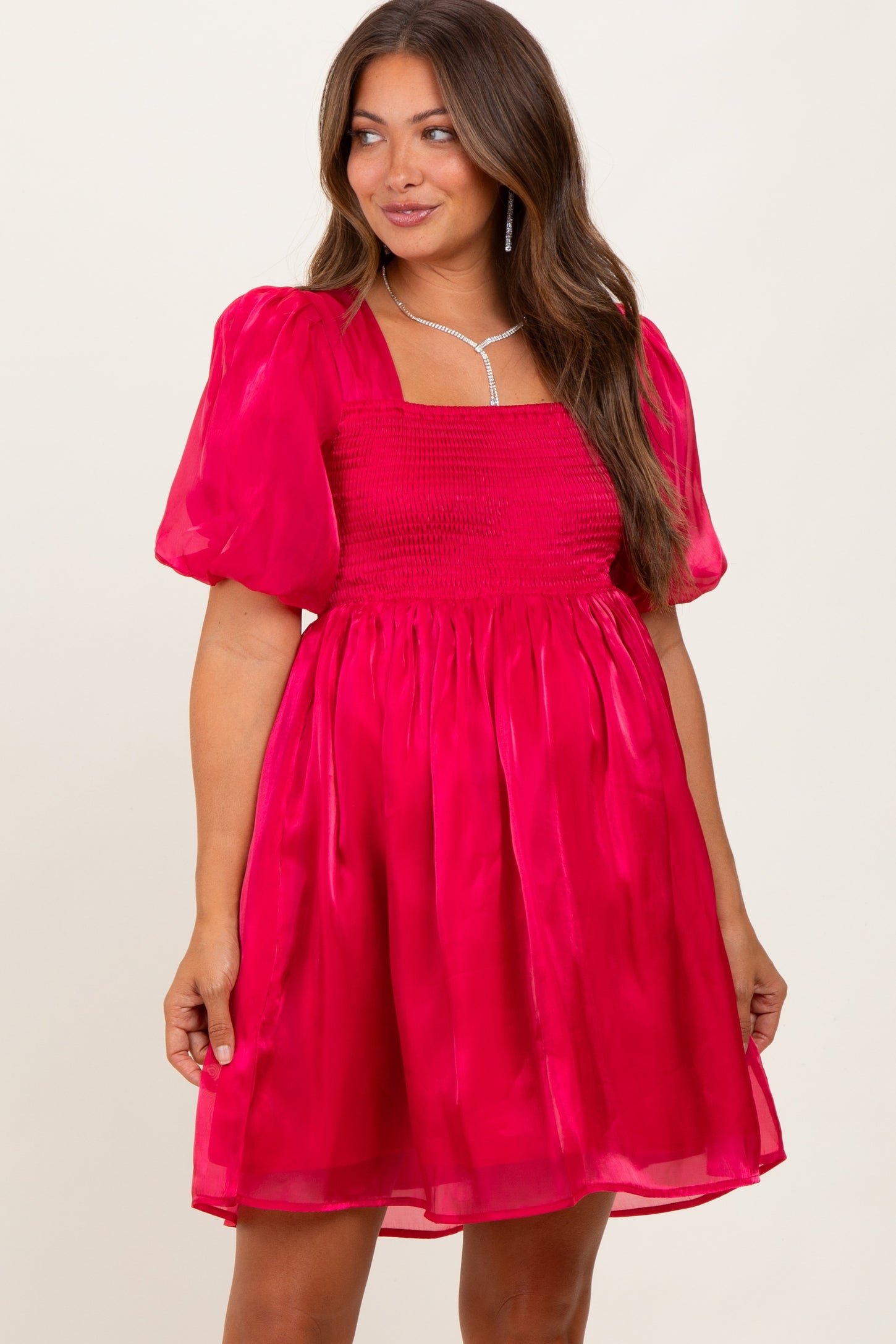 woman wearing a bright pink puff sleeve maternity dress with a smocked bodice and flowy skirt