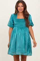 woman wearing a teal maternity dress with puff sleeves and a smocked bodice, showcasing a baby bump