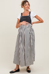 woman wearing a black and white striped maternity dress with denim overalls and holding her baby bump