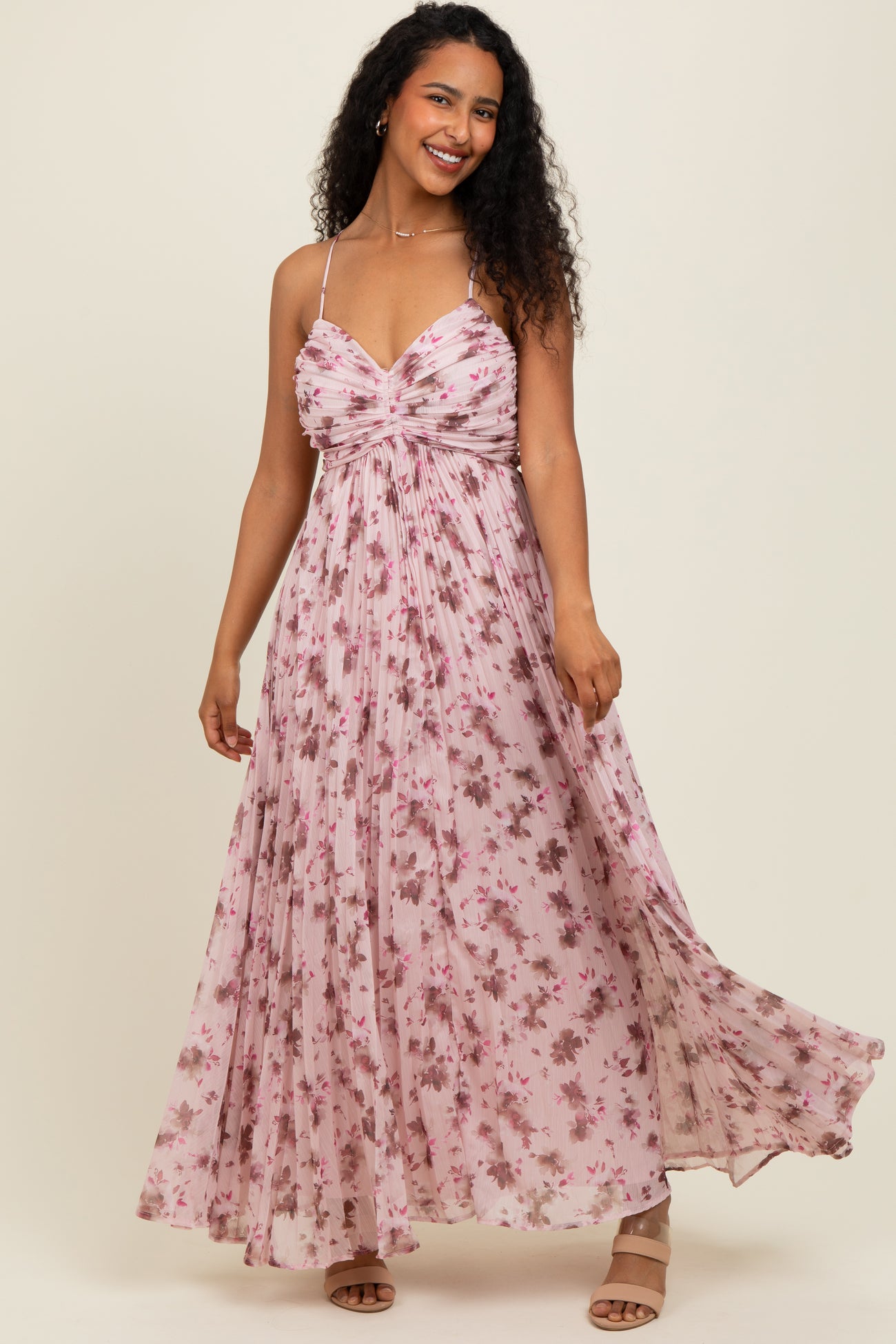 woman wearing a pink floral maxi dress with a ruched bodice and spaghetti straps, smiling at the camera