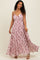 woman wearing a pink floral maxi dress with a ruched bodice and spaghetti straps, smiling at the camera