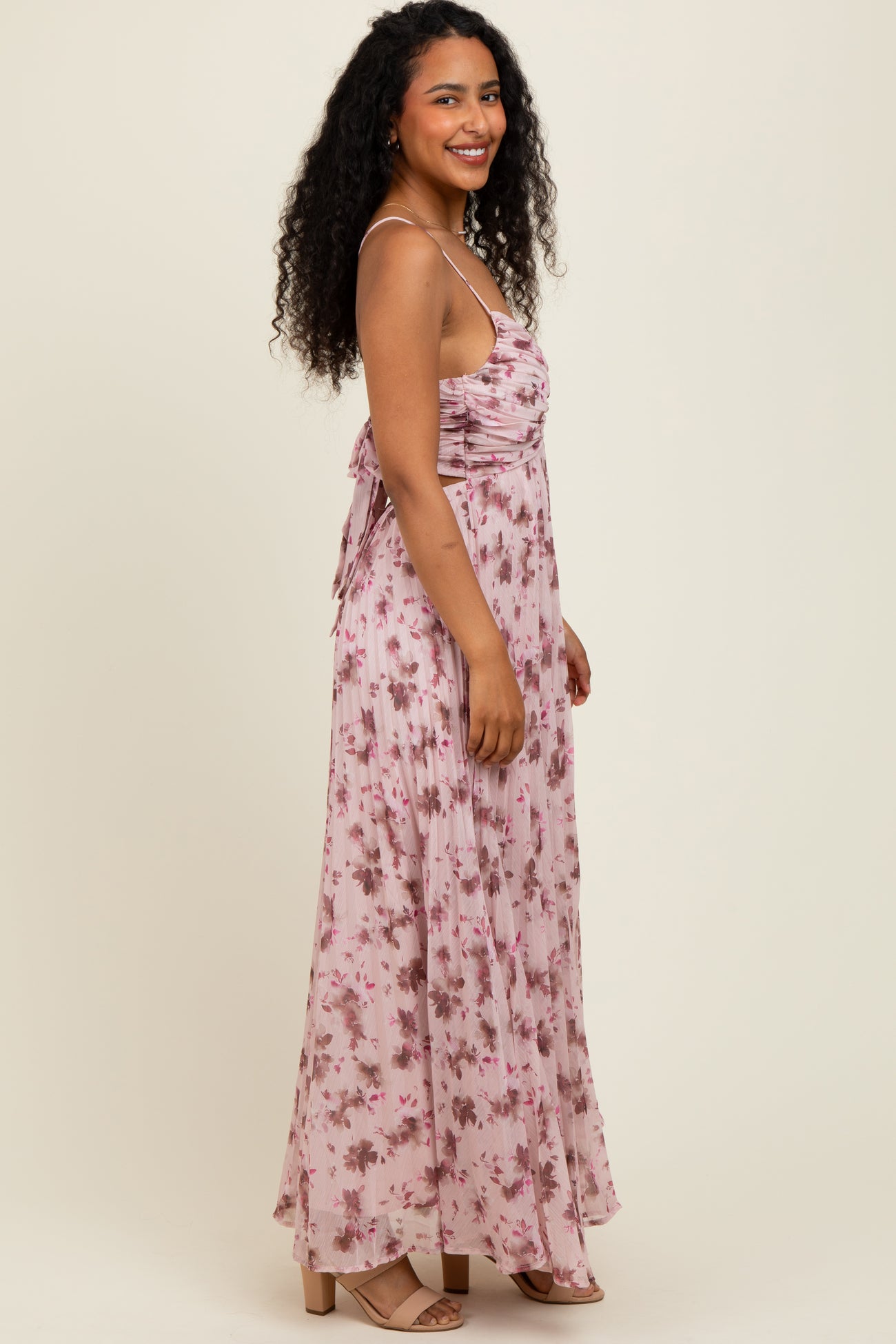 woman wearing a light pink floral maxi dress with spaghetti straps and gathered detailing, standing sideways